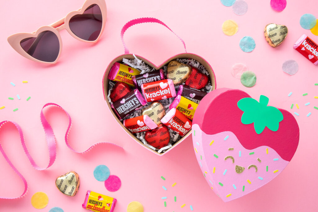 Strawberry heart box is propped open and filled with chocolate candies.