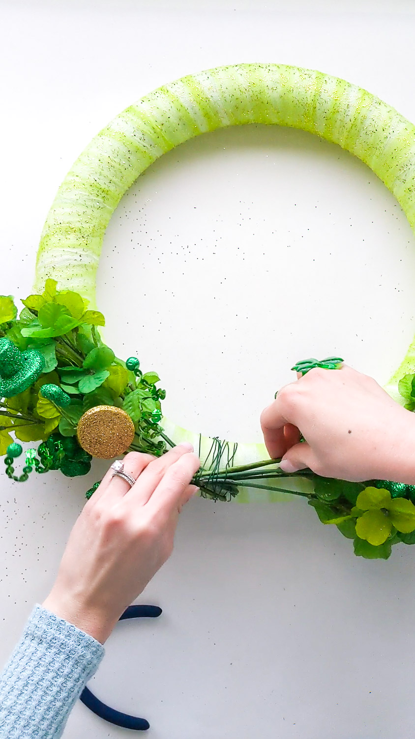Inserting shamrock spray pick under the floral wire attached to the wreath.