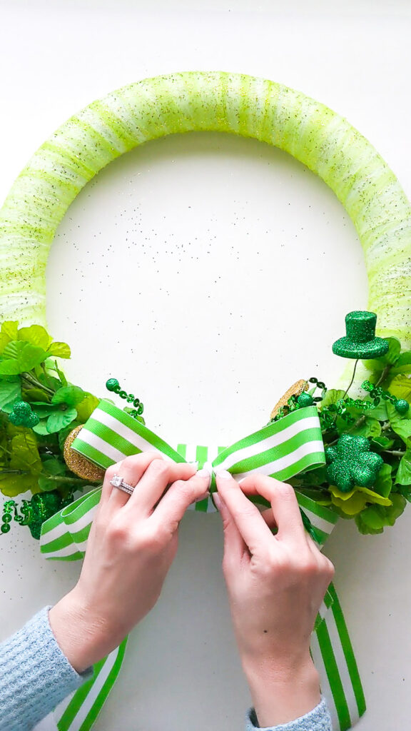 Attaching a green striped bow to the bottom of the shamrock wreath.