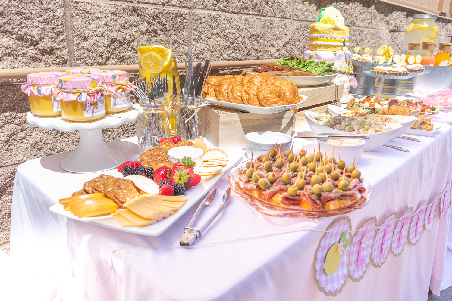 A variety of brunch foods spread out on a long pink table. 