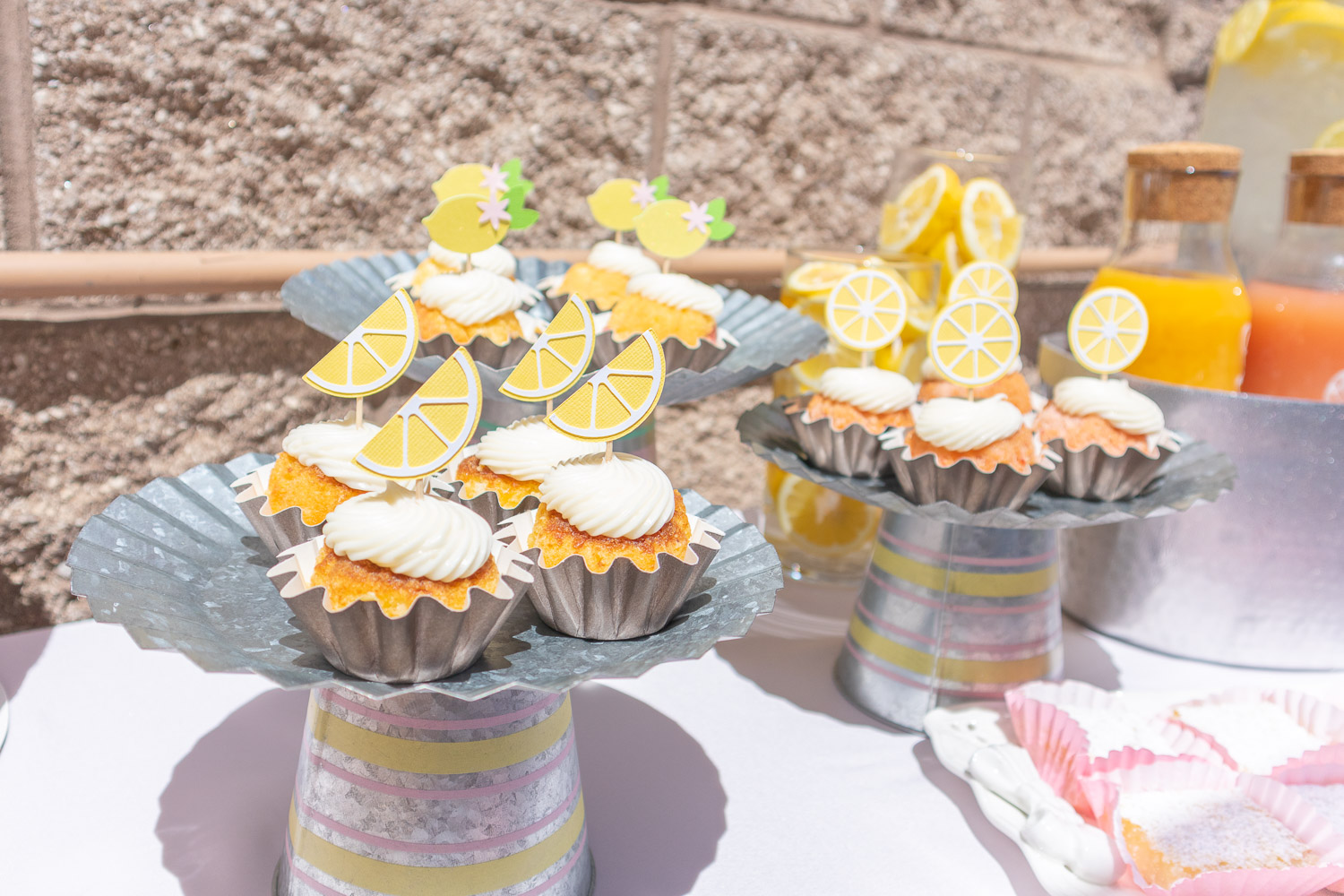 Tiny bundt cakes with paper lemon toppers. They're placed on metal cake stands of different heights.