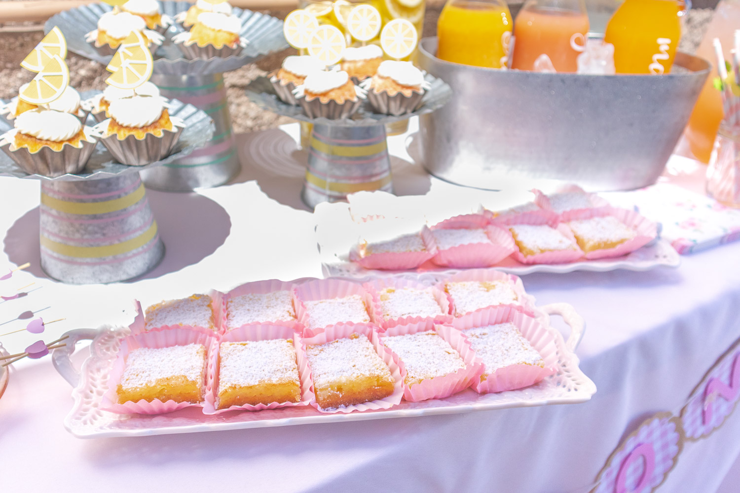 Lemon bars in pink paper wrappers on porcelain tea serving trays. 