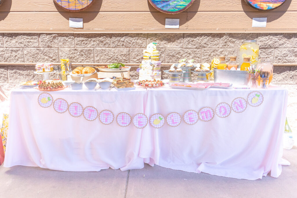 Lemon baby shower food table dressed up with pink tablecloth and handmade paper "Little Lemon" banner.