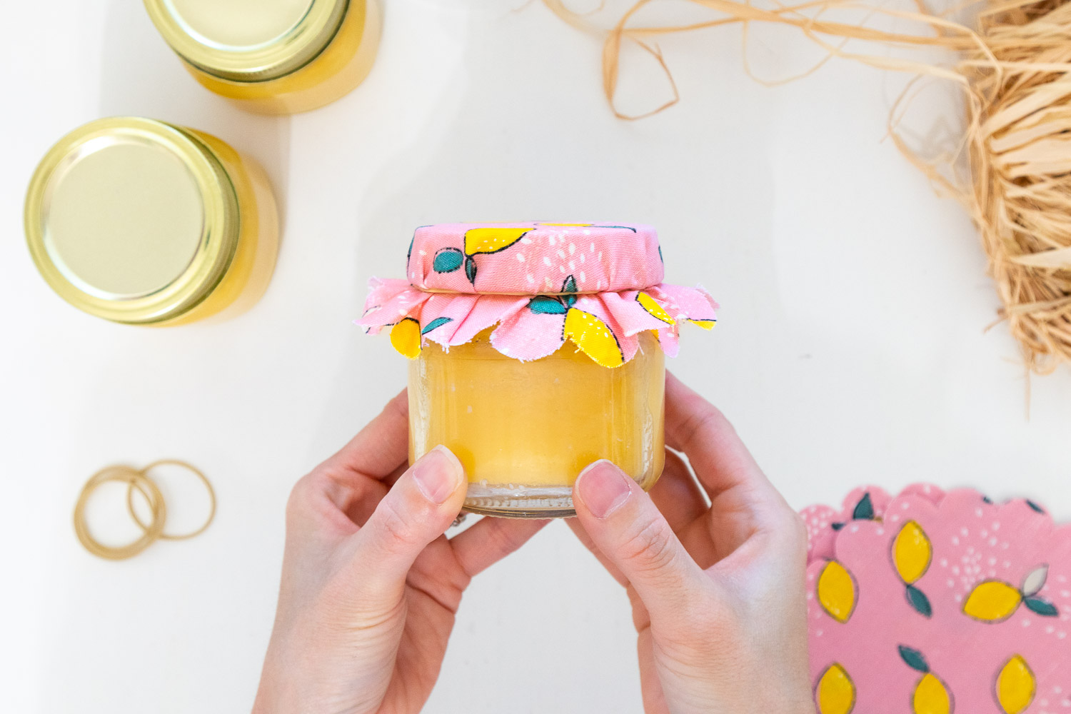 Placing a rubber band to secure the scalloped fabric circle to the neck of the lemon curd jar.