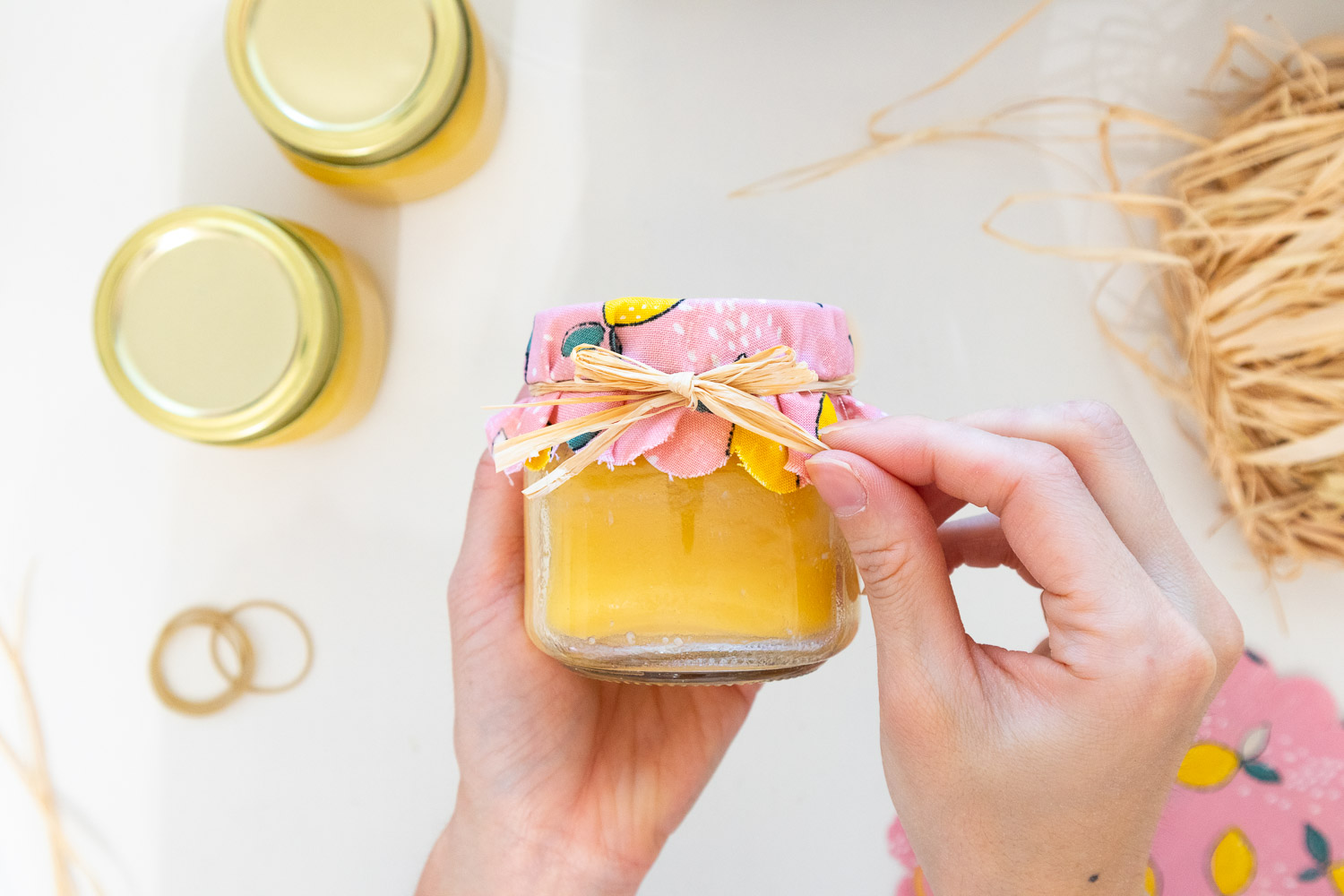 Tying raffia in a bow over lemon curd jar.