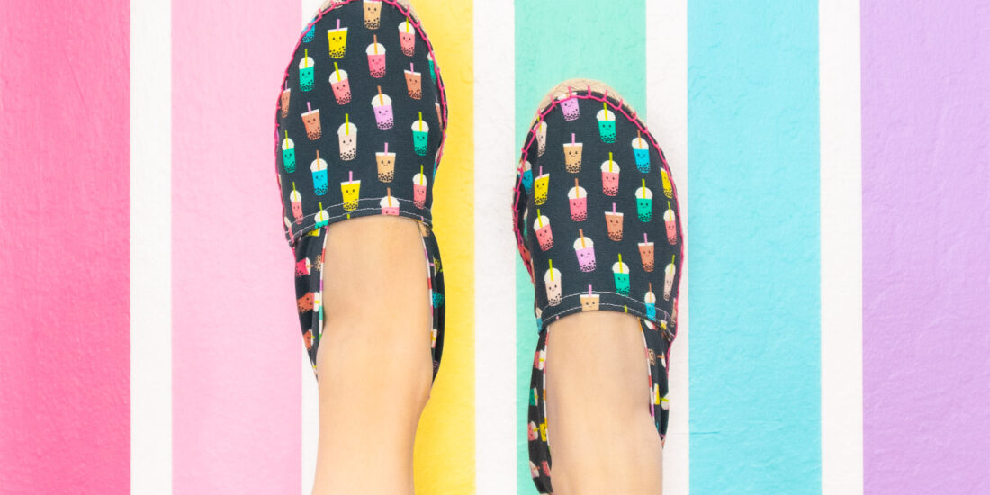 Espadrille shoes with navy background and colorful bubble tea print. They are worn by Blaire, the creator of Freshly Fuji and photographed on a pastel rainbow wall.