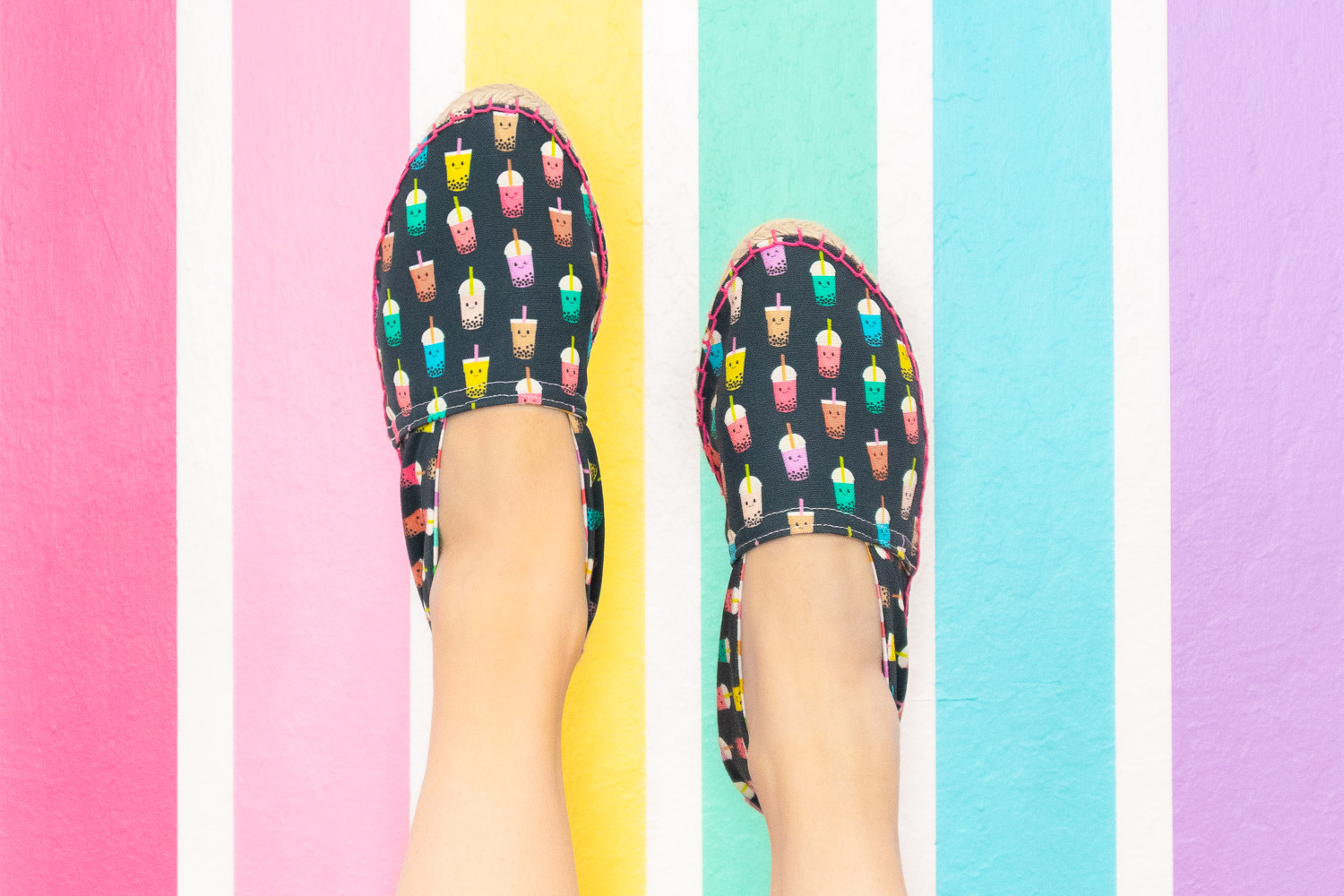 Espadrille shoes with navy background and colorful bubble tea print. They are worn by Blaire, the creator of Freshly Fuji and photographed on a pastel rainbow wall.