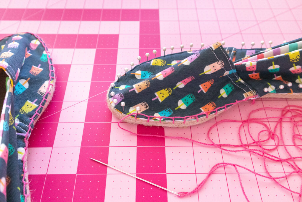 Close-up of blanket stitch along the edge of espadrilles. The shoes are navy with multi-colored boba drinks printed, The shoes are placed on a pink fiskars cutting mat.