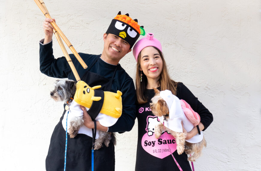 An Asian couple with their two small dogs dressed as Sanrio Sushi. The man is wearing a Badtz Maru chef costume, the woman is wearing a Hello Kitty x Kikkoman soy sauce costume. The gray, terrier mix dog is wearing a Gudetama tamago (egg) sushi costume. The tan Yorkie is wearing an ebi (shrimp) sushi costume.