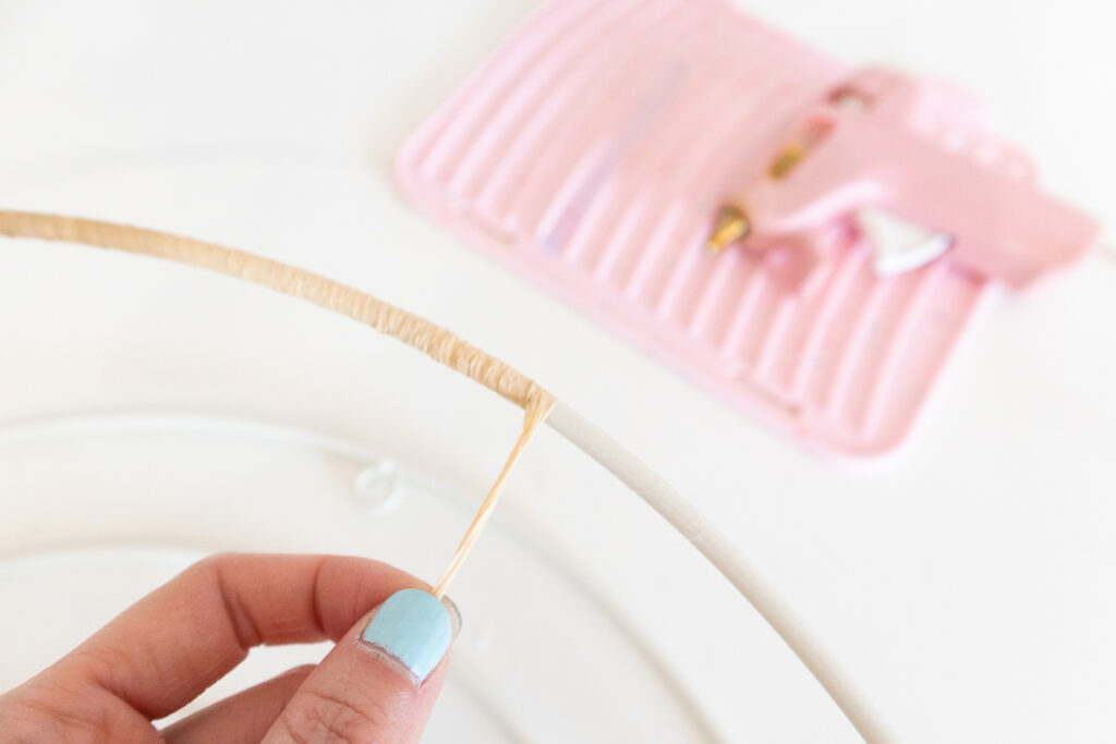 The wire part of the rainbow shelf is being wrapped with a light tan colored raffia strand.