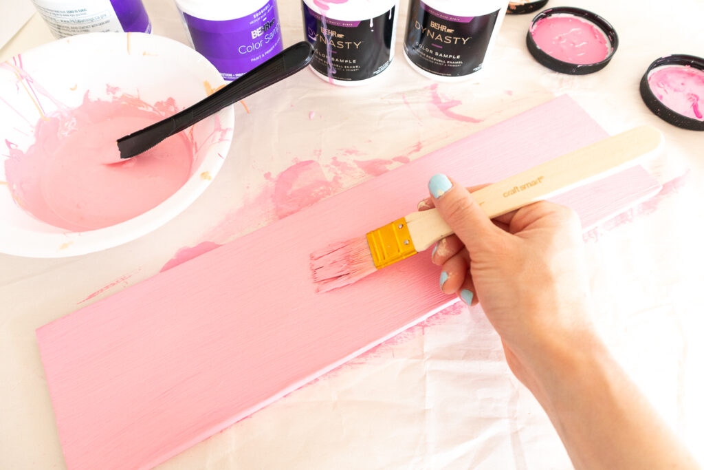 The wood part of the rainbow shelf is being painted a coral pink color.