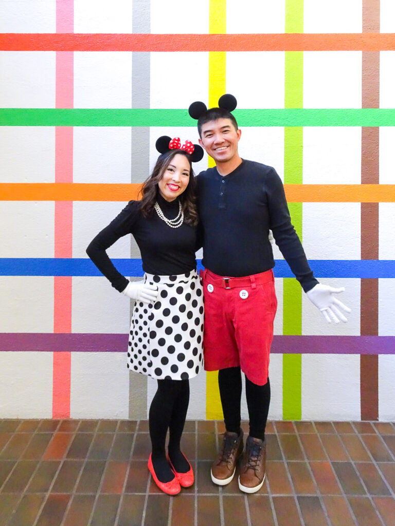 An Asian couple dressed as Mickey and Minnie Mouse in front of a colorful grid wall at the Color Factory.